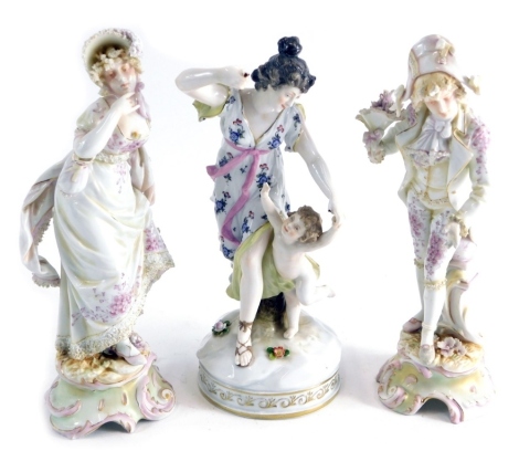 An early 20thC Volkstedt porcelain figure of a gentleman, a further porcelain figure of a lady, polychrome decorated with blue cross sword marks beneath, 25cm high, and another Volkstedt figure group putti and figure of a lady, on a gilt lined base. (3)