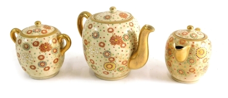 A three piece Japanese Satsuma pottery tea service, comprising teapot, two handled sugar bowl, and milk jug, each profusely decorated with flowers, on a cream ground with gilt highlights, the teapot, 15cm high, unmarked. (3)