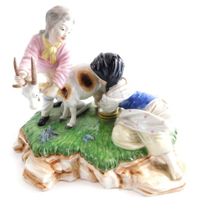 A Continental porcelain figure group of children milking goat, polychrome decorated predominantly in green, pink and brown, with blue circle cross mark beneath, 15cm high.