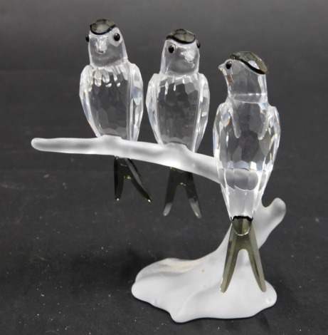 A Swarovski Crystal figure group of three birds, on a frosted glass tree bough, with black glass highlights, swan mark beneath, 9cm high.