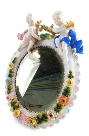 A 20thC Sitzendorf porcelain table mirror of oval form with bevelled glass profusely decorated with an outer border of garlands and flowers in colours and surmounted with two cherubs holding further garlands with bow to the base with plain easel back 30cm