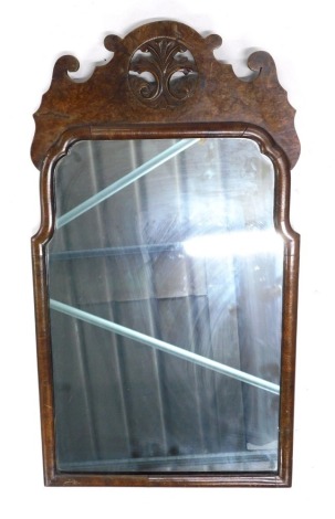 A 20thC walnut framed mirror, with shaped glass, surmounted by a pierced floral emblem, 64cm x 37cm.