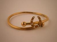 A yellow metal slave type bangle set with a horseshoe with seed pearls and coral