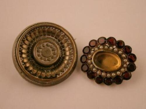 A yellow metal brooch set with red stones bordered by pearls