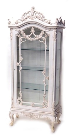 A French style painted cabinet, the arched glass door revealing three shelves surmounted by a scroll and floral moulding, on cabriole legs, 100cm high, 82cm wide, 51cm deep.