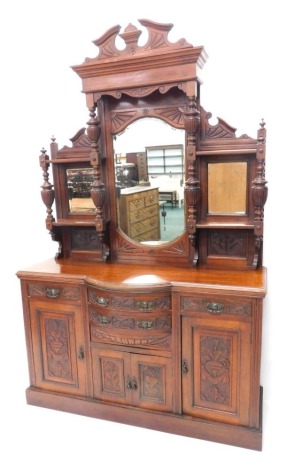 A late 19thC walnut mirror back sideboard, with two drawers and cupboards flanked by further drawers and cupboards, heavily carved with urns and flowers, the upper section with a broken pediment above a shield shaped mirror, flanked by two rectangular bev