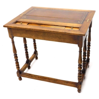 A 20thC oak fold over desk, with a brown leather tooled section with another section for ink bottles and pens, on baluster turned legs, joined by block stretchers with a side draw, when closed 77cm high, 86cm wide, 33cm deep.