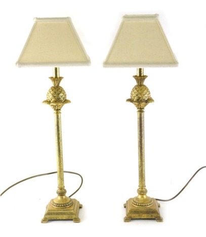 A pair of gilt metal table lamps, with pineapple and fluted stems terminating in step bracket feet with modern shades 71cm high. (2)
