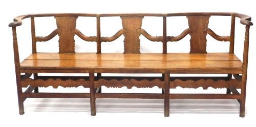 An oak Arts and Crafts style settle, with serpentine back, on turned supports with a carved frieze, on cylindrical stiles, 76cm high, 183cm wide, 51cm deep.