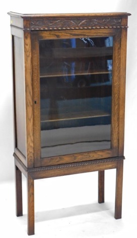 A 20thC oak display cabinet, with carved scroll frieze above a single door revealing two shelves, on square legs, 122cm high, 60cm wide, 32cm deep.