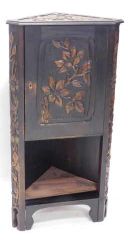 A heavily carved oak Liberty style corner cabinet, decorated with flowers and a poker work back, above an under tier on carved stiles, 101cm high, 51cm wide, 34cm deep.