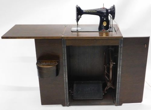 A 20thC Singer treadle sewing machine in oak cabinet, with articulated top and double front doors, 80cm high, 54cm wide, 42cm deep.