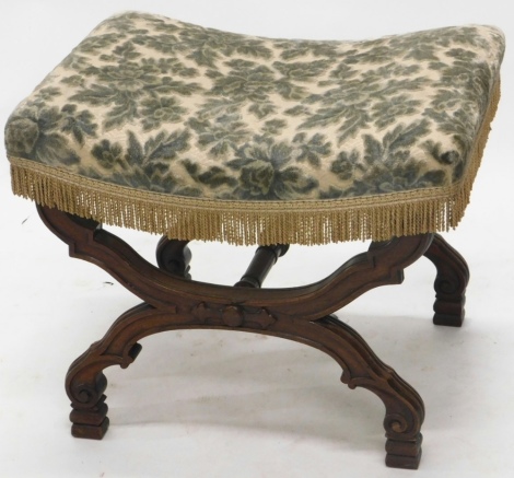 An early 20thC heavily carved Continental stool, with overstuffed seat in floral material, on X shaped legs raised with orbs and scrolls, 52cm high, 66cm wide, 55cm deep.