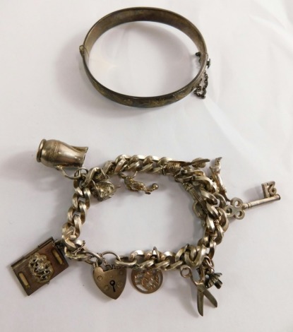 A hinged silver bangle, with vine leaf engraving, and a silver charm bracelet, with British passport, vines, swords and other charms, 79.4g all in.