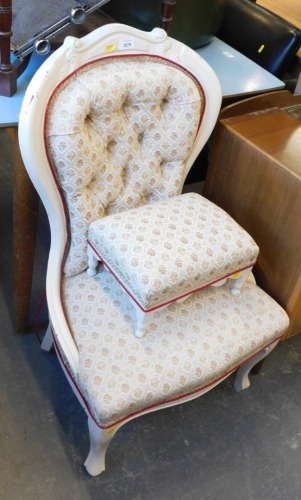 A spoon back chair and footstool, upholstered in floral material, painted in cream.