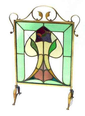 An early 20thC brass Art Nouveau fire screen, with lotus flower coloured glass centre, and scroll outline, on paw feet, 85cm high, 59cm wide, 25cm deep.