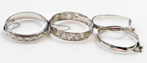 Two silver and foliate engraved bangles, each on a snap clasp with safety chain, a faceted silver bangle, and a further bangle with engraved decoration, 132.6g. (4)