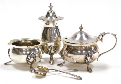 An Edward VII silver three piece cruet, comprising pepper pot, open salt and mustard pot with blue glass liner each piece with a shaped rim raised on three leaf capped hoof feet, together with salt and mustard spoons, Joseph Gloster, Birmingham 1904, weig