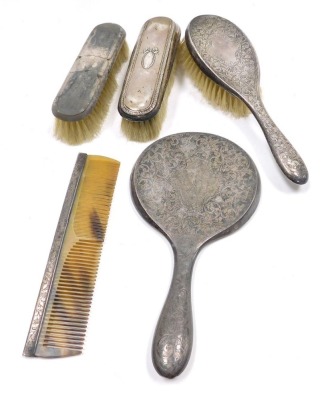 An Edward VII silver backed three piece dressing table set, comprising hand mirror, hair brush and comb, each piece engraved with scrolls and leaves, Chester 1901, together with two further silver backed clothes brushes.