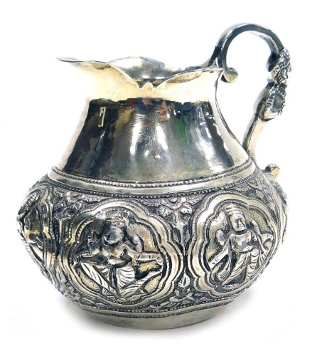 An Indian white metal jug, of bellied form embossed with a band of deities in reserves interspersed with flowers, the handle of scroll form decorated with a half length figure, 8.5cm high, 4.65oz.