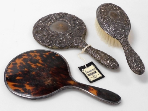 An Elizabeth II silver backed hand mirror and hair brush, each piece embossed with scrolls, leaves and flowers and two faces of the Green Man, Birmingham 1994, together with a silver mounted and tortoiseshell backed hand mirror, Birmingham 1922.