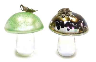 Two iridescent glass mushroom paperweights, possibly by John Ditchfield, one green decorated with an applied silver coloured butterfly, the other mottled purple decorated with an applied silver coloured frog, each 5.5cm high.