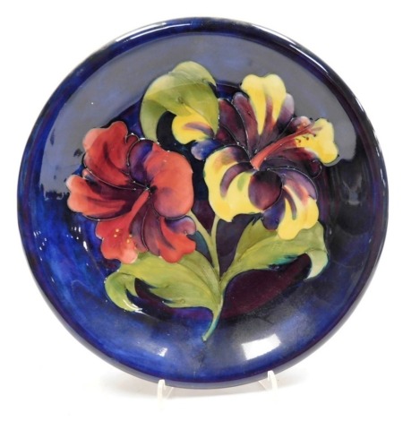 A Moorcroft Hibiscus pattern pottery dish, impressed marks bearing signature and paper label to underside, 22cm diameter.