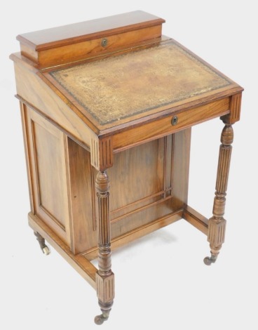 A Victorian walnut Davenport, the top with a hinged lid containing spaces for letters and pens, above a brown tooled leather writing slope, enclosing a birds eye maple fitted interior, the base raised on turned supports, with three drawers to one side, br