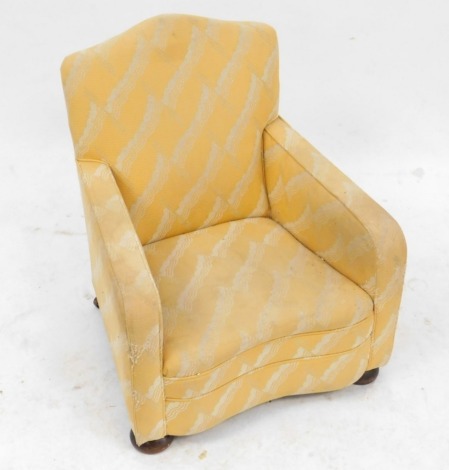 A 1930s child's armchair, upholstered in pale yellow patterned fabric, with a shaped back and front, on bun feet, 65cm high.