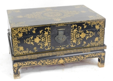 A 20thC Chinese lacquered chest on stand, decorated with gold coloured flowers, etc., with a shaped iron clasp enclosing a red painted interior, 47cm high, 81cm wide, 56cm deep.