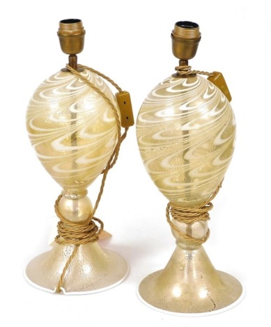 A pair of Continental glass table lamps, the body of elongated globular form, decorated with waves of white and pale yellow against a speckled gold coloured ground, on a conical base, 45.5cm high.