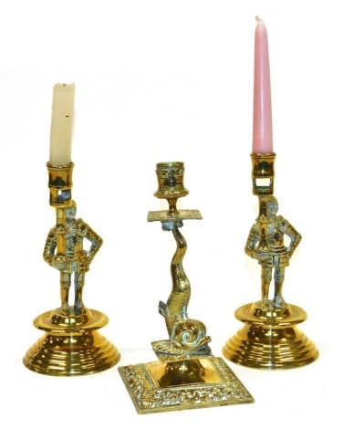 A pair of Victorian brass candlesticks, modelled as a figure in armour holding a taper, each on a circular socle base, 23cm high, together with a 19thC brass candlestick, the stem modelled as a dolphin, on a square base embossed with flowers, 13cm high.