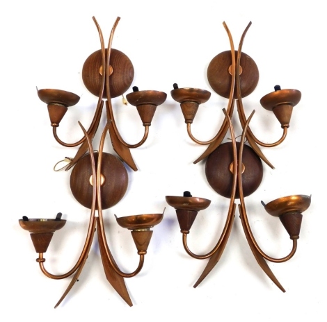 A set of four mid century teak and copper two branch wall lights, the circular wall mount surmounted by two sweeping copper branches, with applied teak kite shaped decoration, each 37cm high.