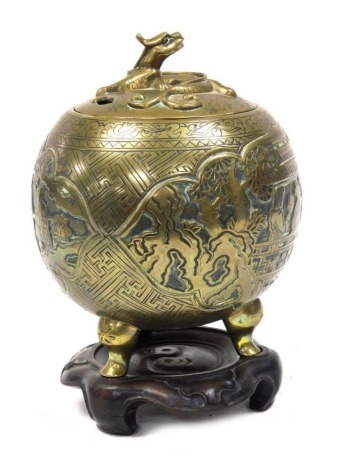 A Qing Dynasty Chinese bronze censer and cover, embossed with reserves of figures in a garden, the lid with a dragon finial, raised on three cabriole legs, with a hardwood stand, 23cm high.