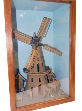 An early 20thC wooden montage, of a windmill, houses, and figures with carts, in a pine and glazed fronted case, case 69cm high, 44cm wide.