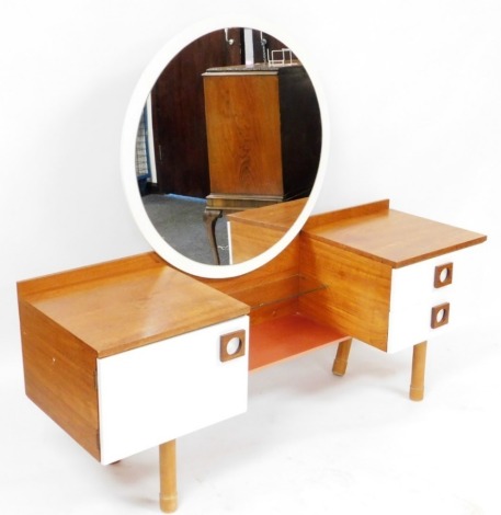 A mid century teak and white laminate dressing table, with a circular mirrored back above a narrow glass shelf and pink metallic coloured lower tier, flanked to each side by a cabinet and two drawers, raised on cylindrical legs, 137cm high, 153cm wide, 47