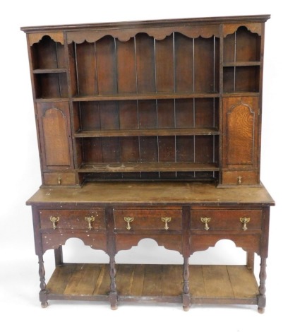 An early 20thC oak dresser, the top with an arrangement of shelves, recesses, cupboards and drawers, the base with three drawers, above a solid pot board raised on turned support with shaped aprons, 128cm high, 149cm wide, 43cm deep.