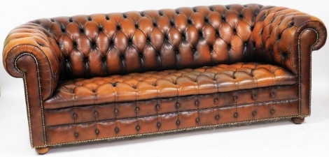 A tan leather three seater Chesterfield sofa, with button back and seat, raised on turned legs, 204cm wide. The upholstery in this lot does not comply with the 1988 (Fire & Fire Furnishing) Regulations, unless sold to a known exporter or upholsterer it wi