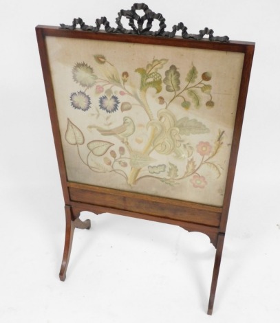 A late Victorian mahogany framed fire screen, with a carved bow surmount, rectangular glazed front with silk work tapestry of a bird, flowers, fruit, nuts, and scrolling leaves, raised on outswept legs, 100cm high, 58cm wide.