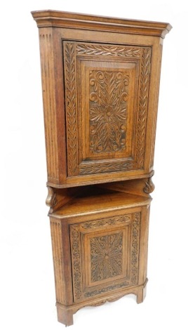 An early 20thC oak corner cupboard, the outswept pediment over a floral and foliate carved panelled door, above a shelf and similarly carved panel door, raised on bracket feet, 183cm high, 72cm wide, 43cm deep.