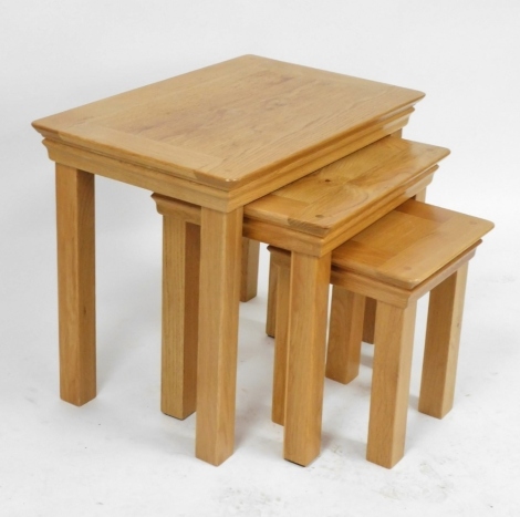 A nest of light oak occasional tables, raised on square legs, largest table 55cm high, 68cm wide, 44cm deep.