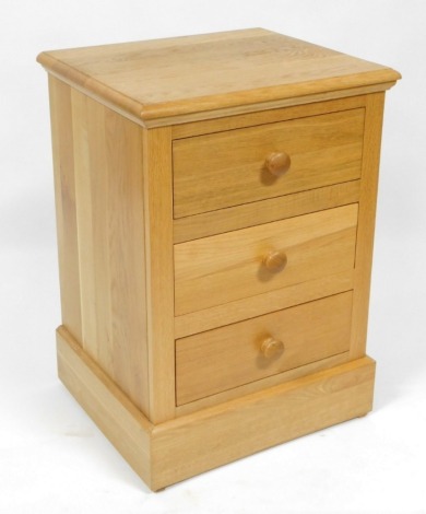 A light oak bedside chest, of three drawers, raised on a plinth base, 74cm high, 53cm wide, 46cm deep.