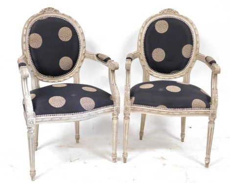 A pair of 19thC style grey painted open armchairs, with carved floral and foliate detailing, patterned black circular back and serpentine seat, raised on fluted legs, 60cm wide. The upholstery in this lot does not comply with the 1988 (Fire & Fire Furnish