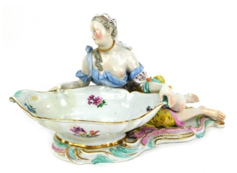 A 19thC Meissen porcelain figural sweetmeat dish, modelled as a partially clad lady holding a large scalloped bowl, polychrome decorated with rococo base, crossed swords mark in blue, 32cm wide. (AF, restored and repaired)