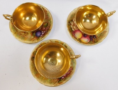 A set of three Aynsley Orchard Gold pattern tea cups and saucers, each painted with fruit by N Brunt,with a gold lustre internal finish, with green stamp to underside, the saucers 15cm diameter, the cups 6cm high. (6) - 3