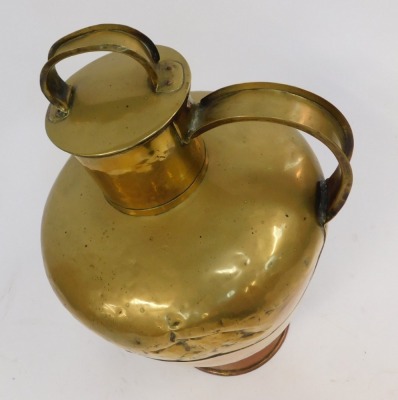 A 19thC brass lidded flagon, with a formed handle and strap top, on a copper foot, 70cm high. (AF) - 2