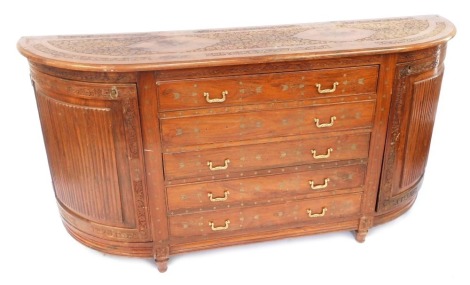 An Indian hardwood and brass inlaid side cabinet, the top decorated with flowers, etc., above an arrangement of five drawers flanked by curved doors with raised fluted panels, on turned tapering legs, 91cm high, 178cm wide, 45cm deep.