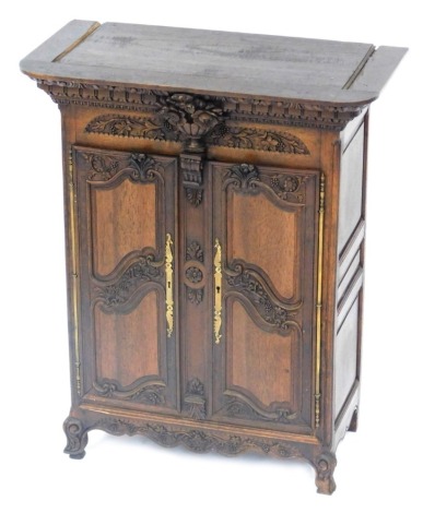 A 19thC French miniature walnut armoire, with a carved shaped cornice, a leaf carved frieze centred by a vase of flowers, above two elaborately decorated doors enclosing sliding velvet lined trays possibly for jewellery, on shaped bracket feet, 52cm high,