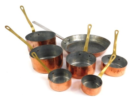 A graduated set of six copper saucepans, with brass handles, together with a copper frying pan with a stainless steel handle.