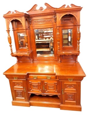 A late Victorian mahogany breakfront sideboard, the triple break arch pediments with foliate carving, above a dentil moulding, the central panel carved with fruit and flowers, inset rectangular bevelled glass plate, flanked by two further bevelled glass r